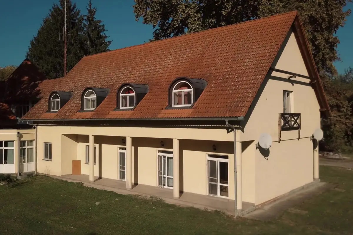 Sárga falú, piros tetős épületszárny íves tetőablakokkal