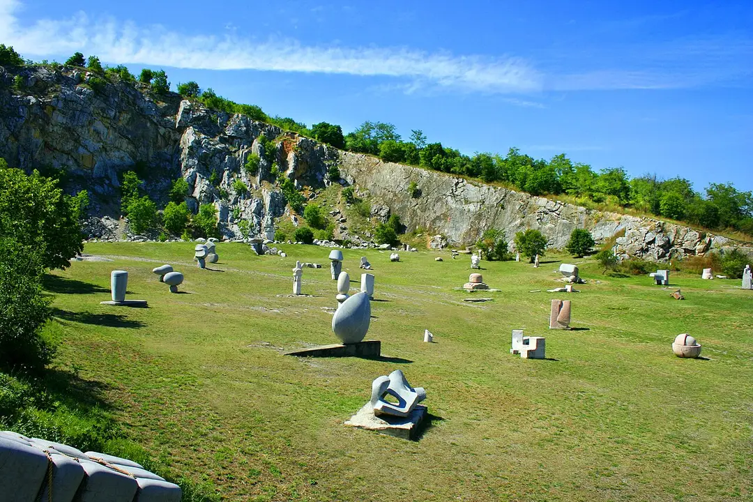 Kőszobrok a nagyharsányi szoborpark füvén, mögöttük a kőbánya sziklafala